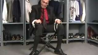 Online film SUG Tuxedo clad man tied to chair ball gagged and struggling.